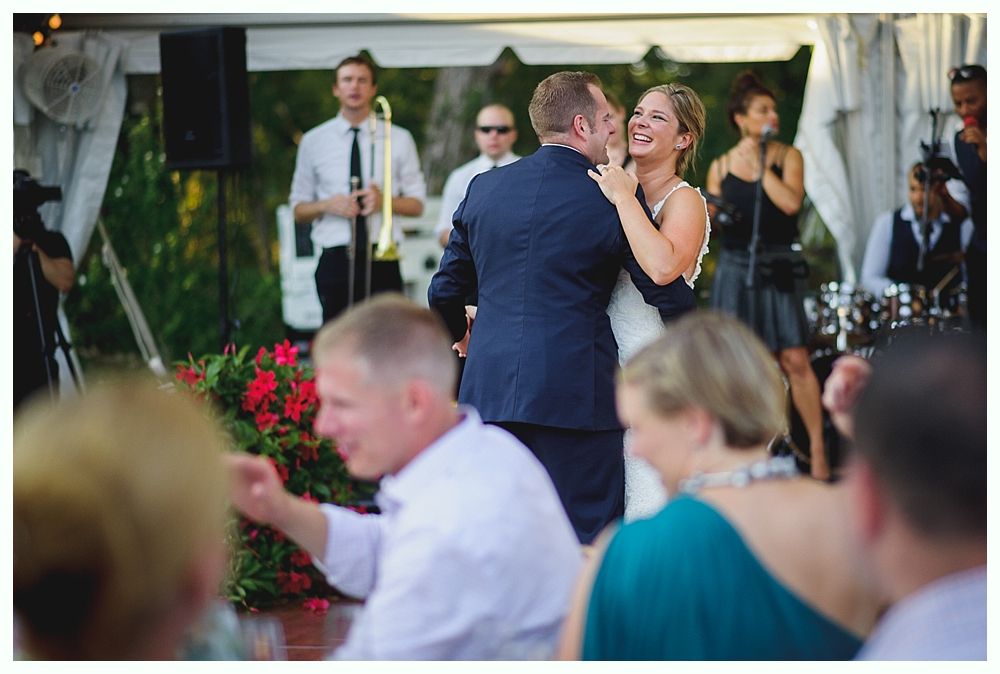 Bride with arms up, making a funny face, groom looking at his hand, cake cutting in background.