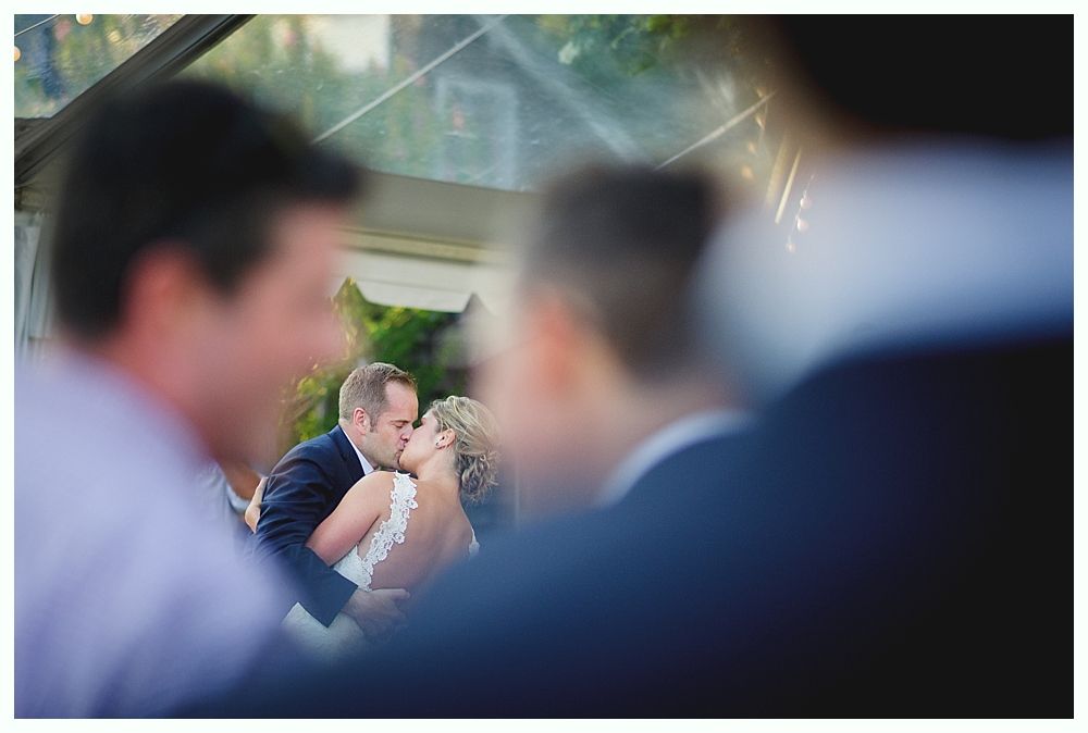 Bride with arms up, making a funny face, groom looking at his hand, cake cutting in background.