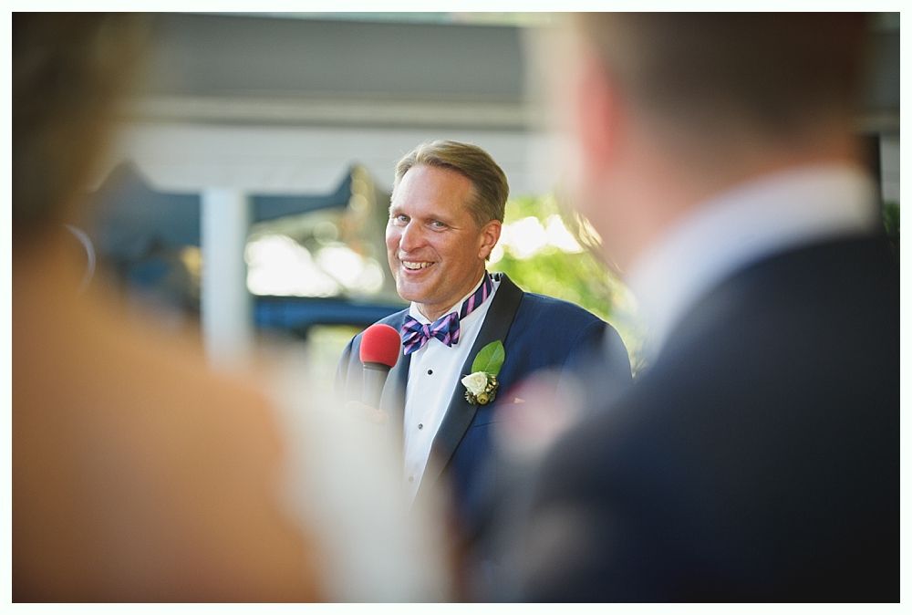 Bride with arms up, making a funny face, groom looking at his hand, cake cutting in background.