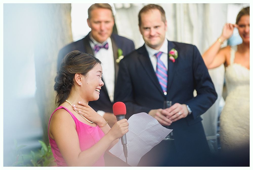 Bride with arms up, making a funny face, groom looking at his hand, cake cutting in background.