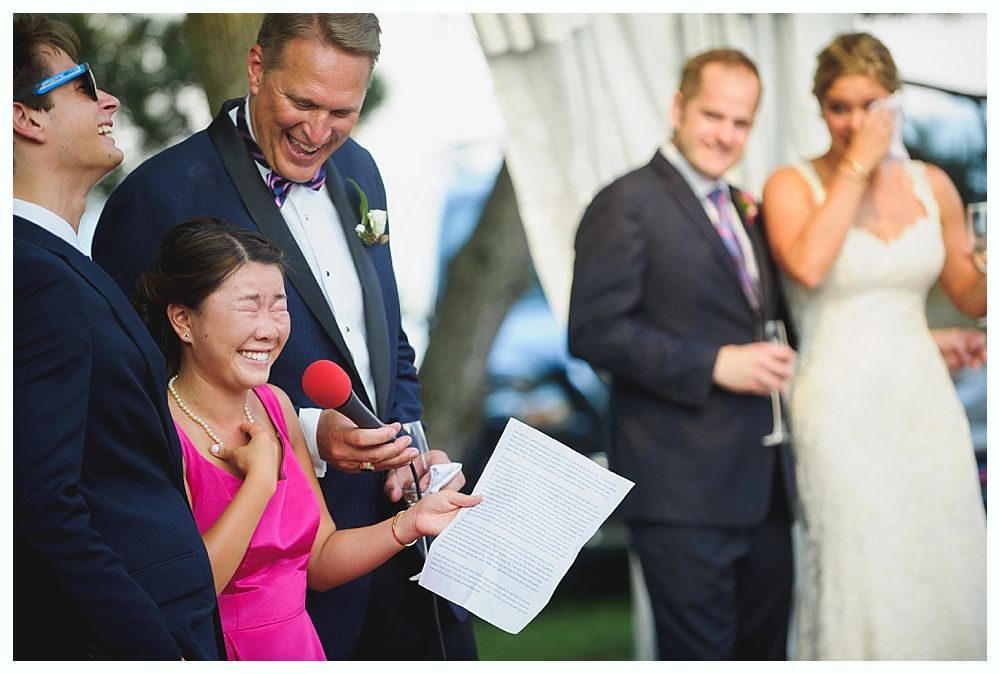 Bride with arms up, making a funny face, groom looking at his hand, cake cutting in background.