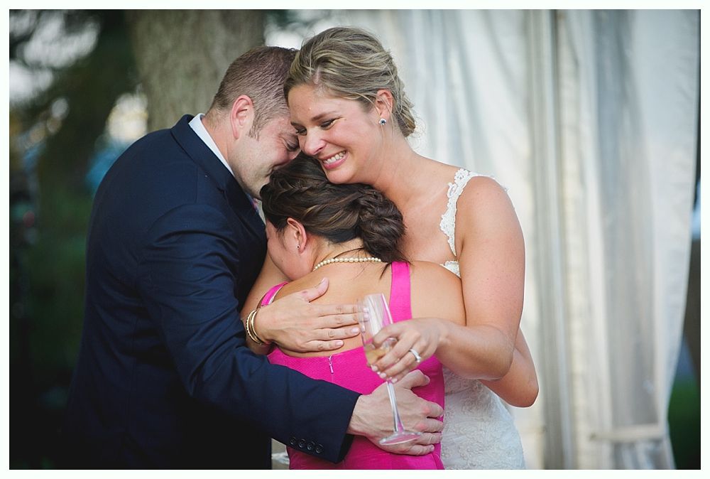 Bride with arms up, making a funny face, groom looking at his hand, cake cutting in background.