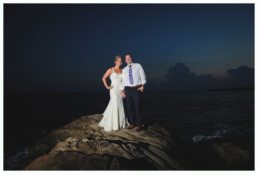 Bride with arms up, making a funny face, groom looking at his hand, cake cutting in background.