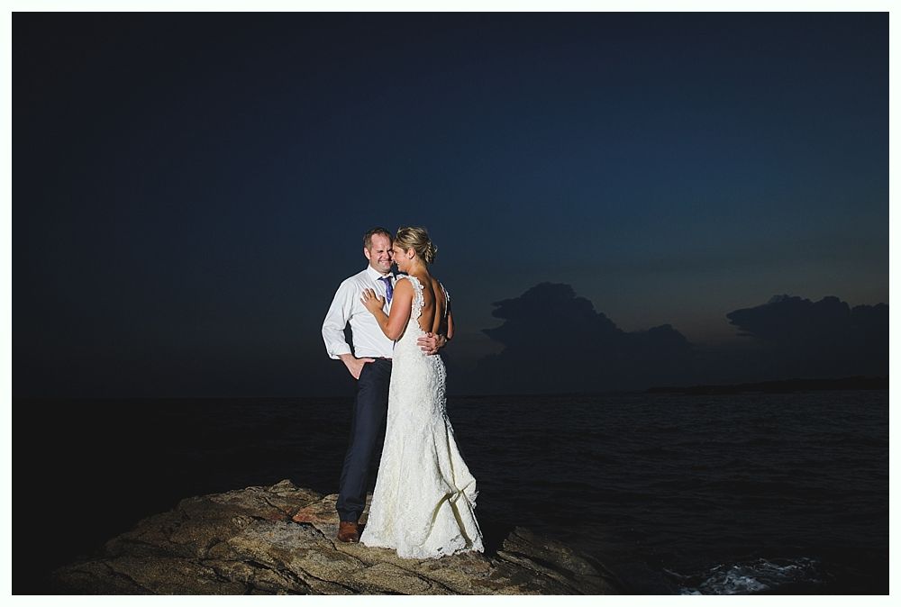 Bride with arms up, making a funny face, groom looking at his hand, cake cutting in background.