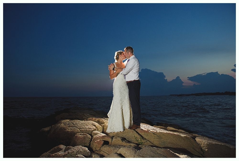Bride with arms up, making a funny face, groom looking at his hand, cake cutting in background.