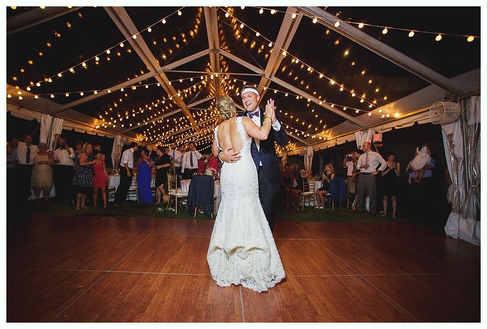 Bride with arms up, making a funny face, groom looking at his hand, cake cutting in background.