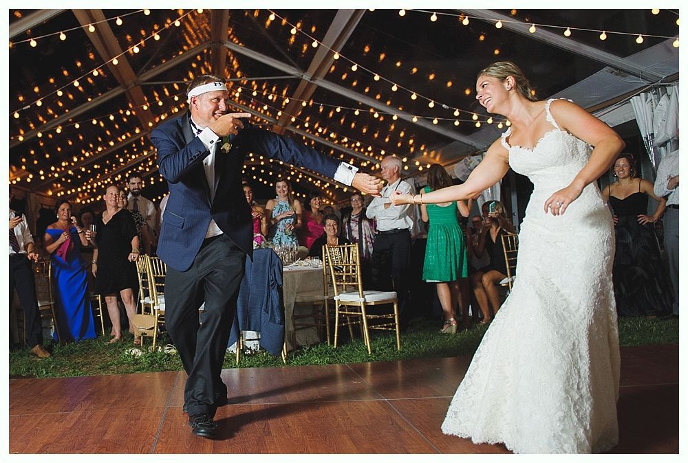 Bride with arms up, making a funny face, groom looking at his hand, cake cutting in background.