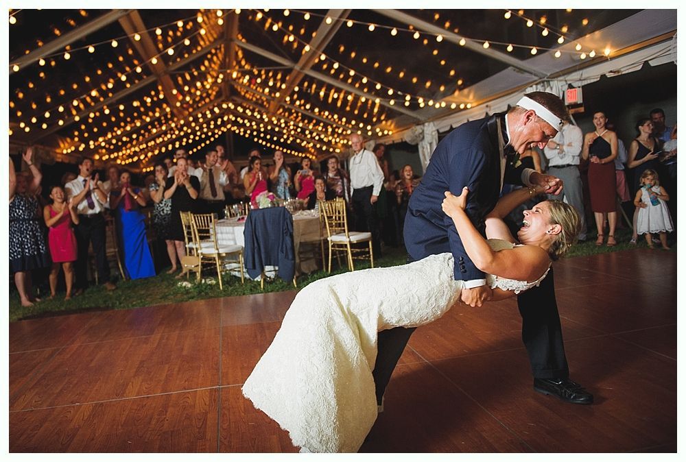 Bride with arms up, making a funny face, groom looking at his hand, cake cutting in background.