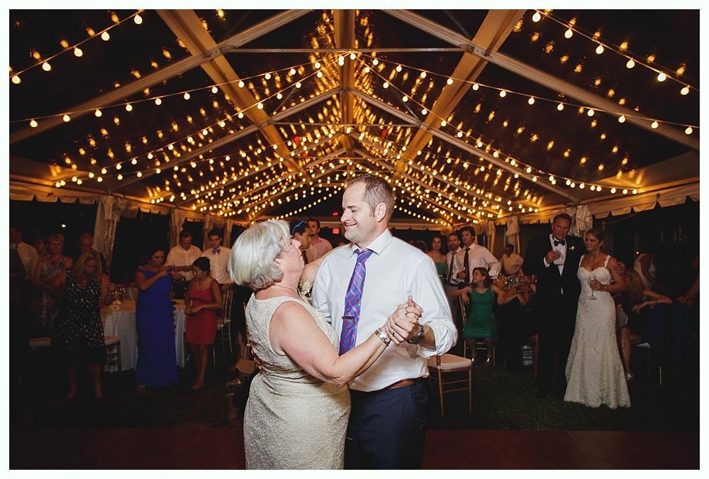 Bride with arms up, making a funny face, groom looking at his hand, cake cutting in background.