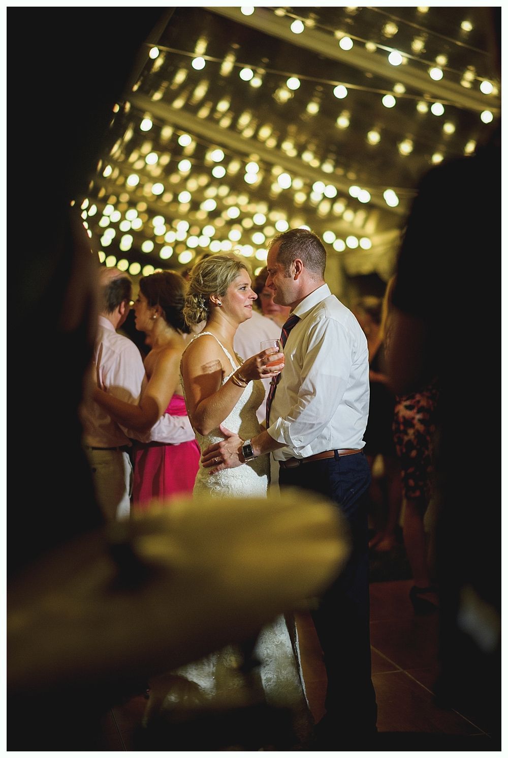 Bride with arms up, making a funny face, groom looking at his hand, cake cutting in background.