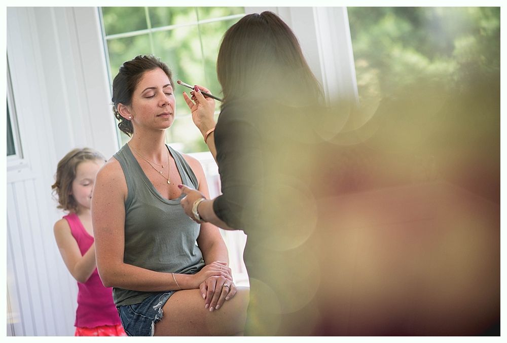 Couple on boardwalk by ocean, framed by beach plants under a blue sky with clouds.
