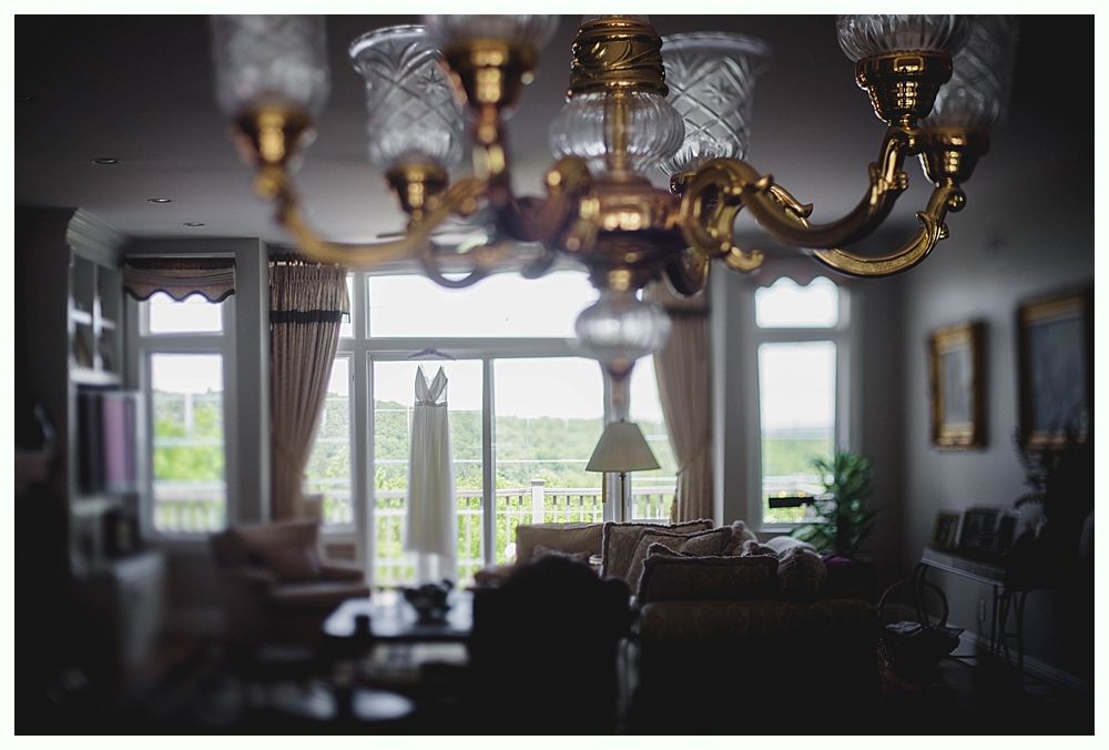 Bride in white gown holding bouquet, posed outdoors. Sunlight streams through trees.