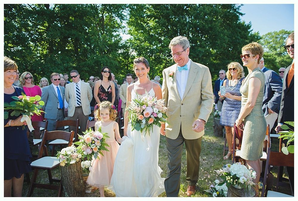 Bride with arms up, making a funny face, groom looking at his hand, cake cutting in background.