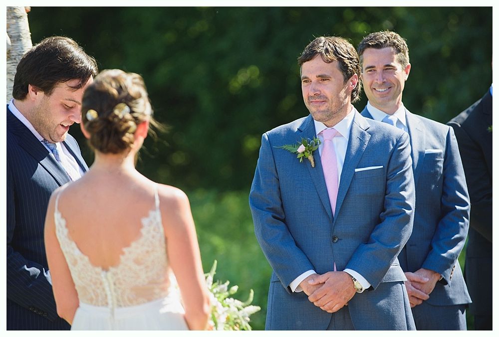 Bride with arms up, making a funny face, groom looking at his hand, cake cutting in background.