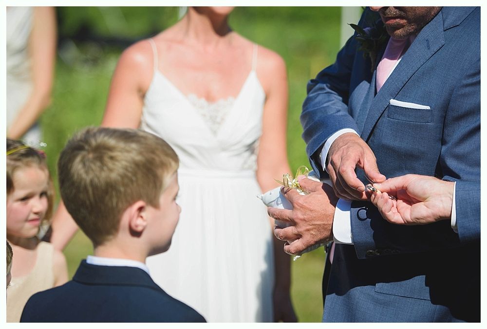 Bride with arms up, making a funny face, groom looking at his hand, cake cutting in background.