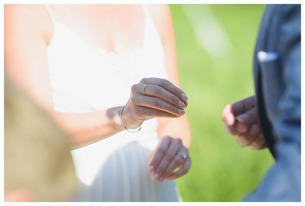 Bride with arms up, making a funny face, groom looking at his hand, cake cutting in background.