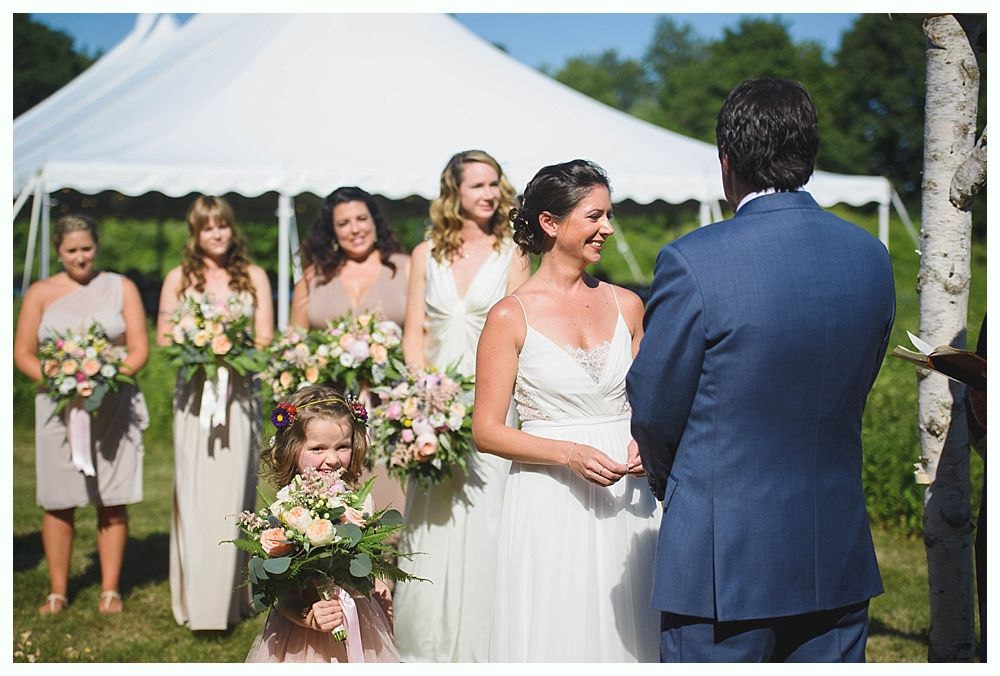 Bride with arms up, making a funny face, groom looking at his hand, cake cutting in background.