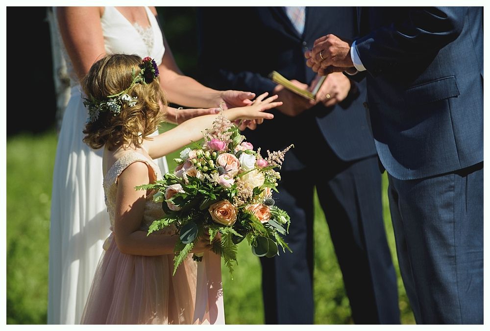Bride with arms up, making a funny face, groom looking at his hand, cake cutting in background.