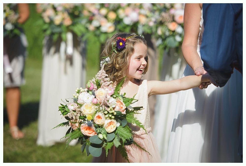 Bride with arms up, making a funny face, groom looking at his hand, cake cutting in background.