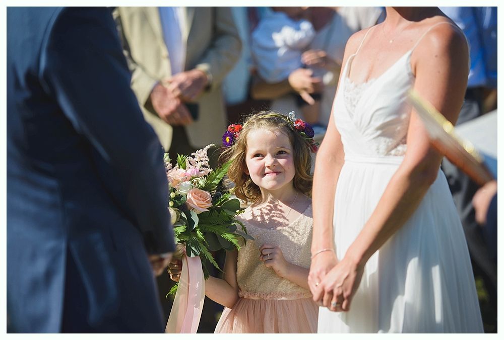 Bride with arms up, making a funny face, groom looking at his hand, cake cutting in background.