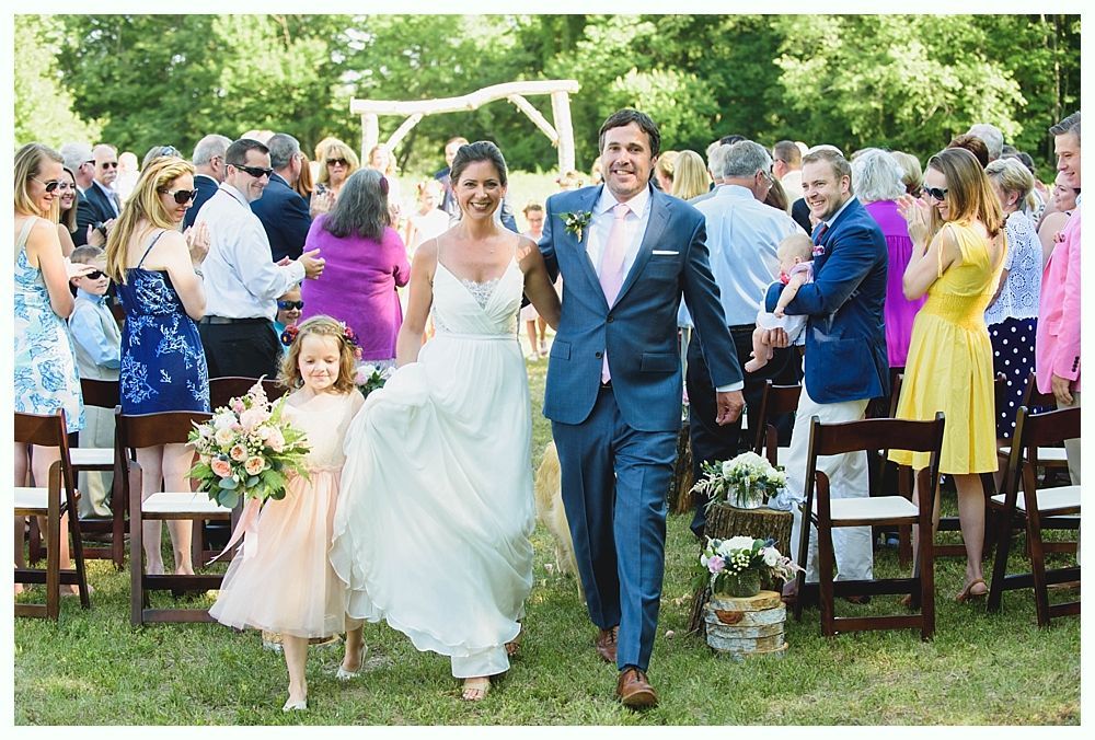 Bride with arms up, making a funny face, groom looking at his hand, cake cutting in background.