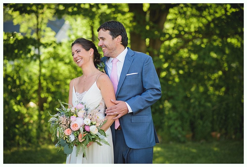 Bride with arms up, making a funny face, groom looking at his hand, cake cutting in background.