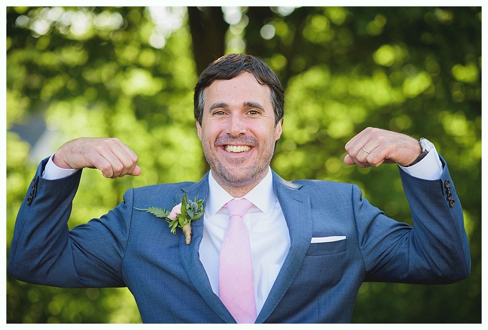 Bride with arms up, making a funny face, groom looking at his hand, cake cutting in background.