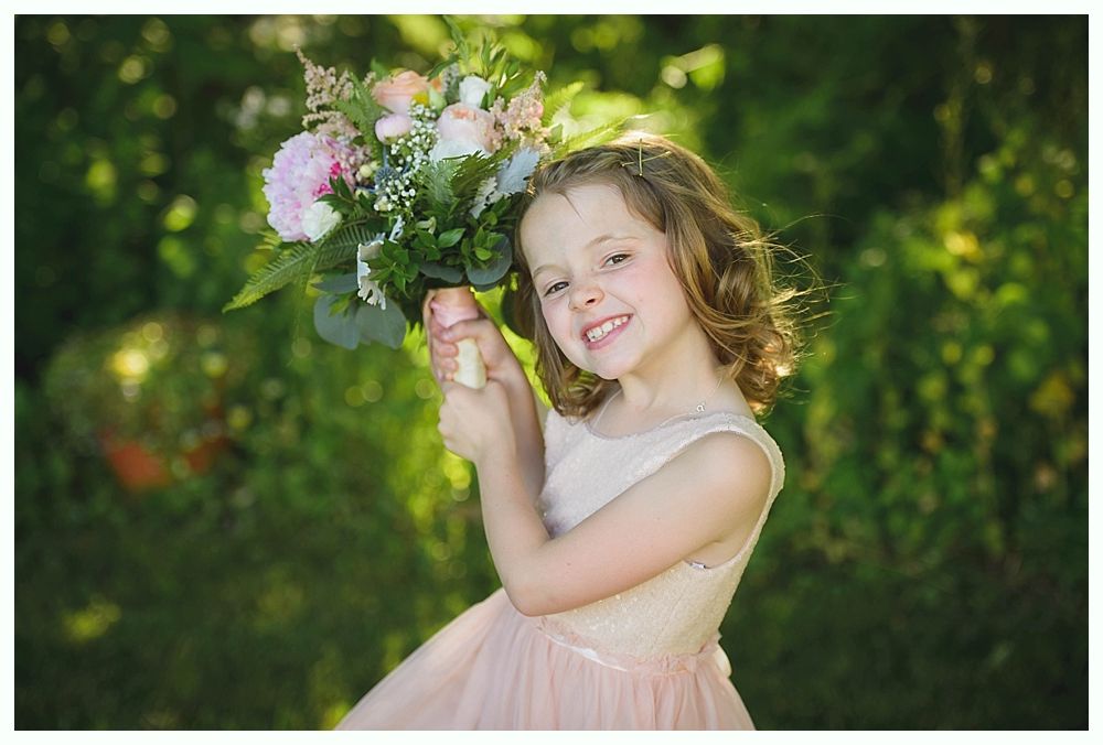 Bride with arms up, making a funny face, groom looking at his hand, cake cutting in background.