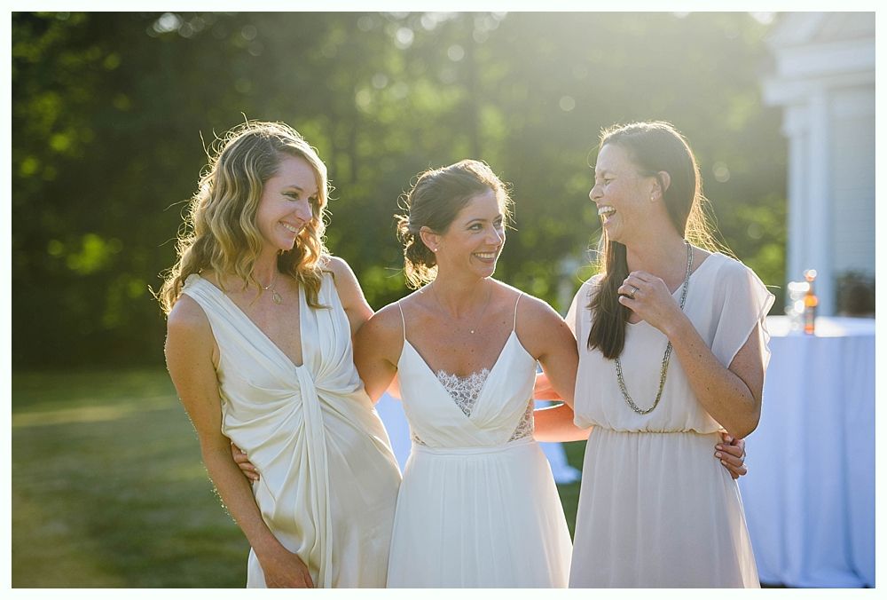Bride with arms up, making a funny face, groom looking at his hand, cake cutting in background.