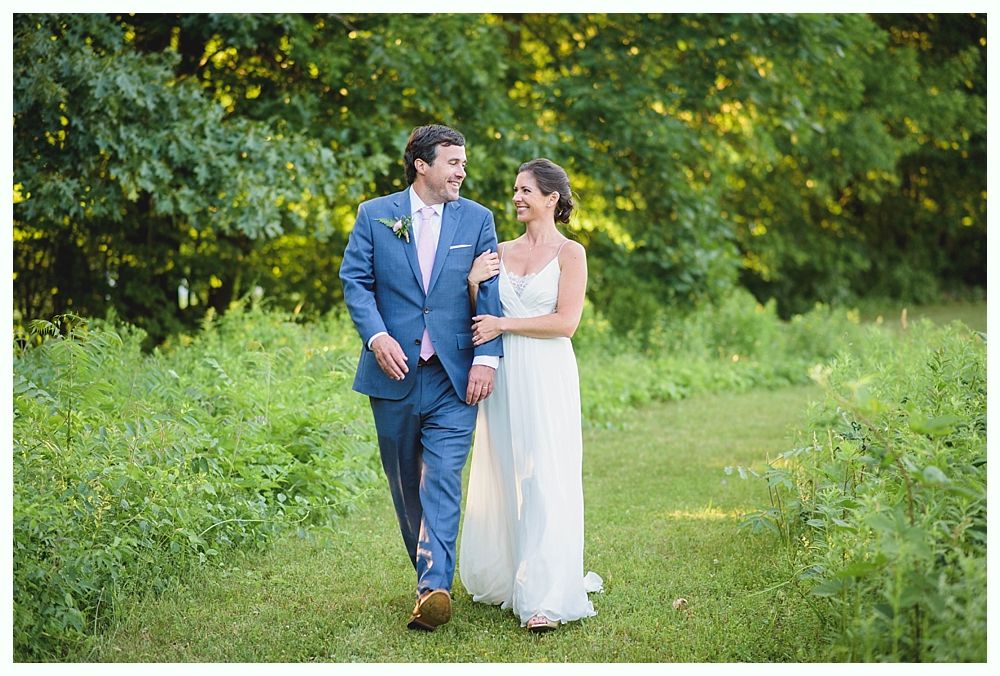 Bride with arms up, making a funny face, groom looking at his hand, cake cutting in background.