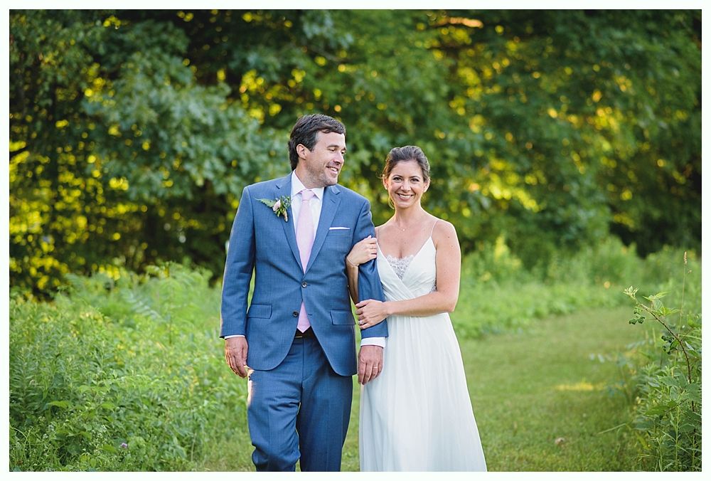 Bride with arms up, making a funny face, groom looking at his hand, cake cutting in background.