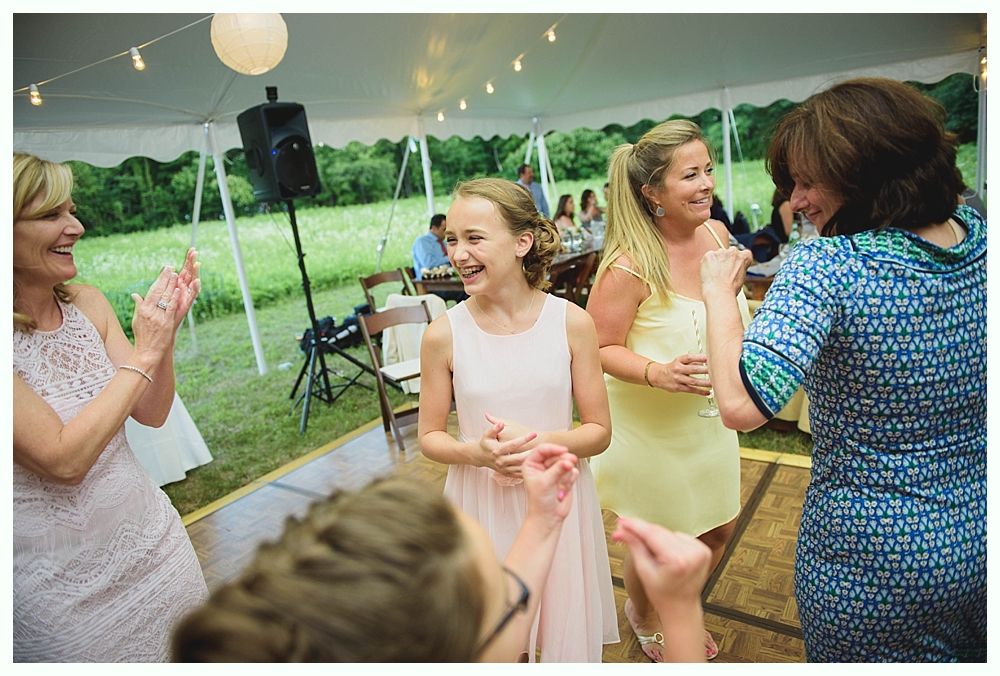 Bride with arms up, making a funny face, groom looking at his hand, cake cutting in background.