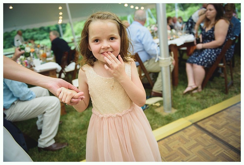 Bride with arms up, making a funny face, groom looking at his hand, cake cutting in background.