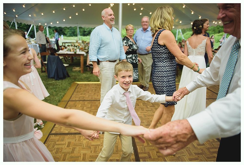 Bride with arms up, making a funny face, groom looking at his hand, cake cutting in background.