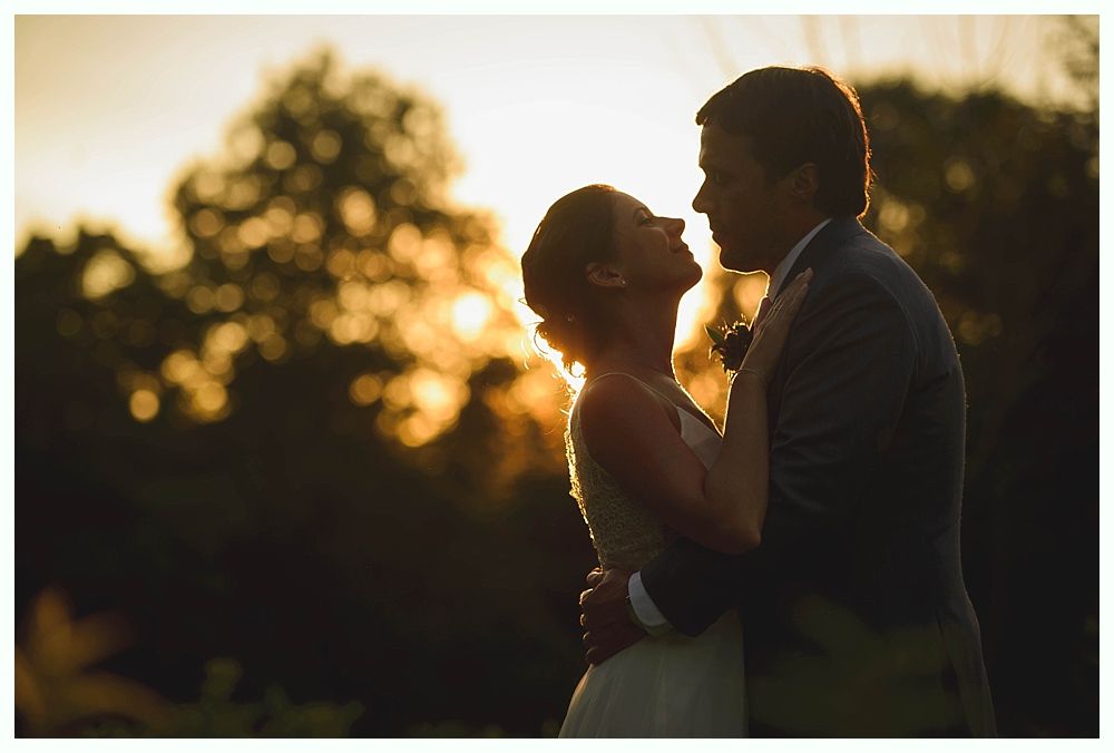 Bride with arms up, making a funny face, groom looking at his hand, cake cutting in background.