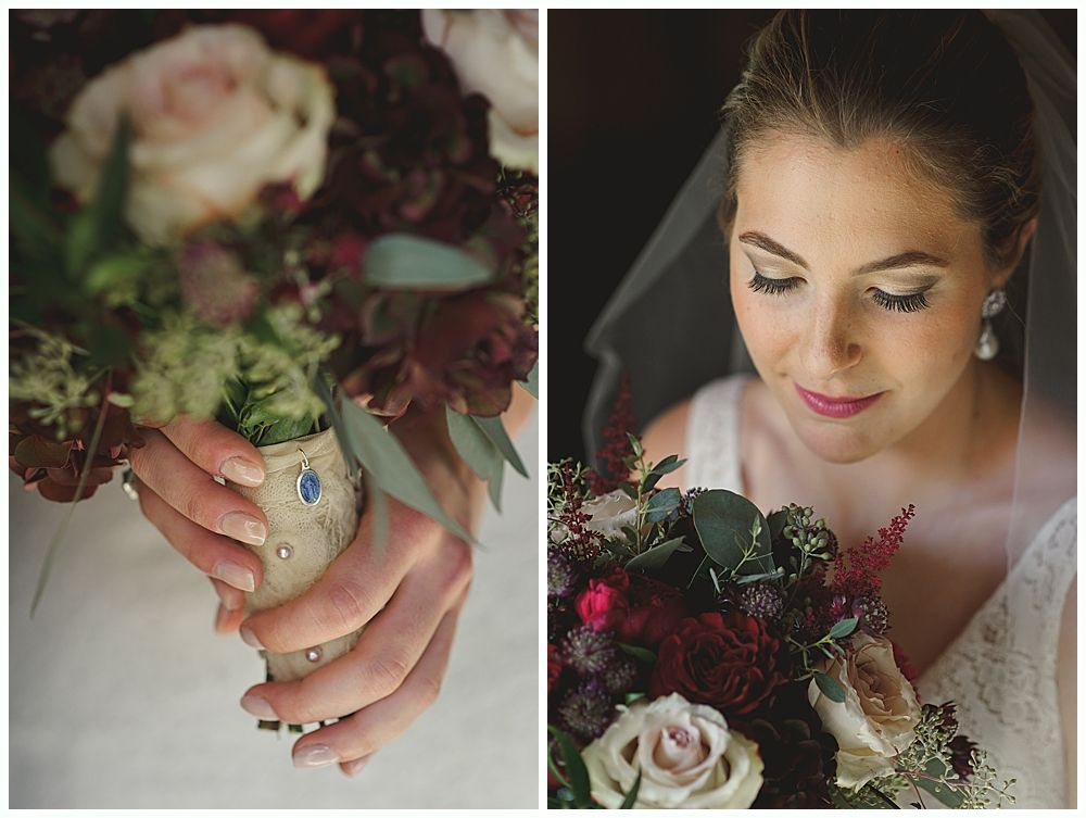 Bride holding bouquet; burgundy, cream, and green flowers. She looks down, lit by soft light.