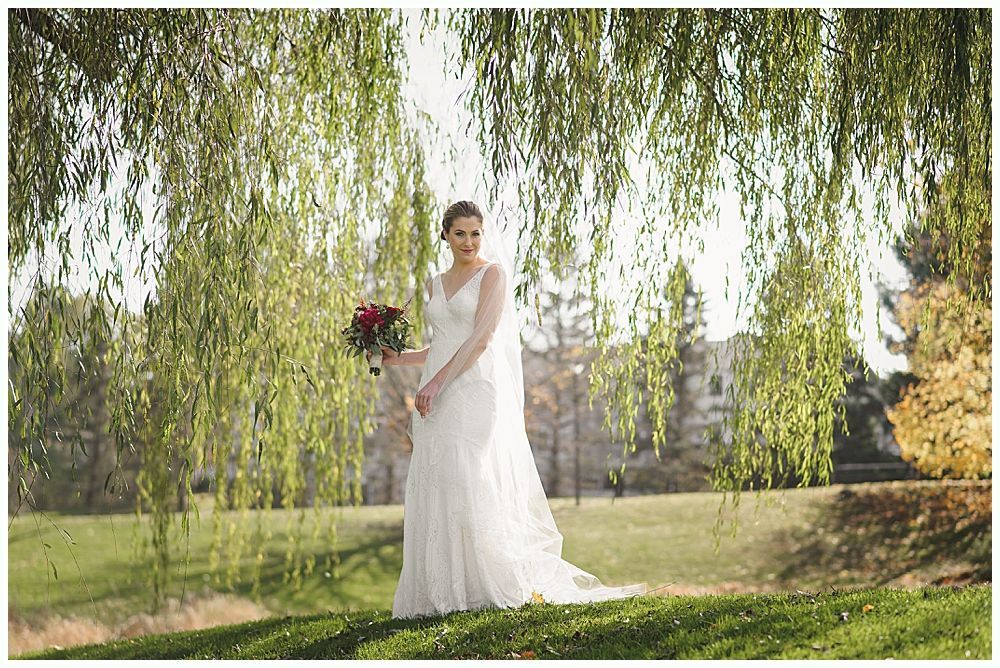 Bride in white dress holding bouquet, standing under weeping willow.