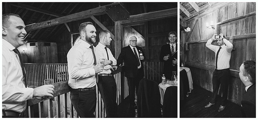 Men in a wooden building, some holding drinks, one toasting. Black and white.