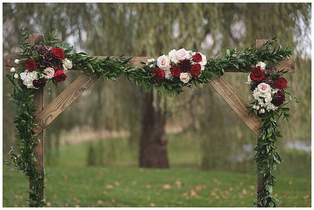 Wooden wedding arch decorated with greenery and red and white flowers, outdoors.