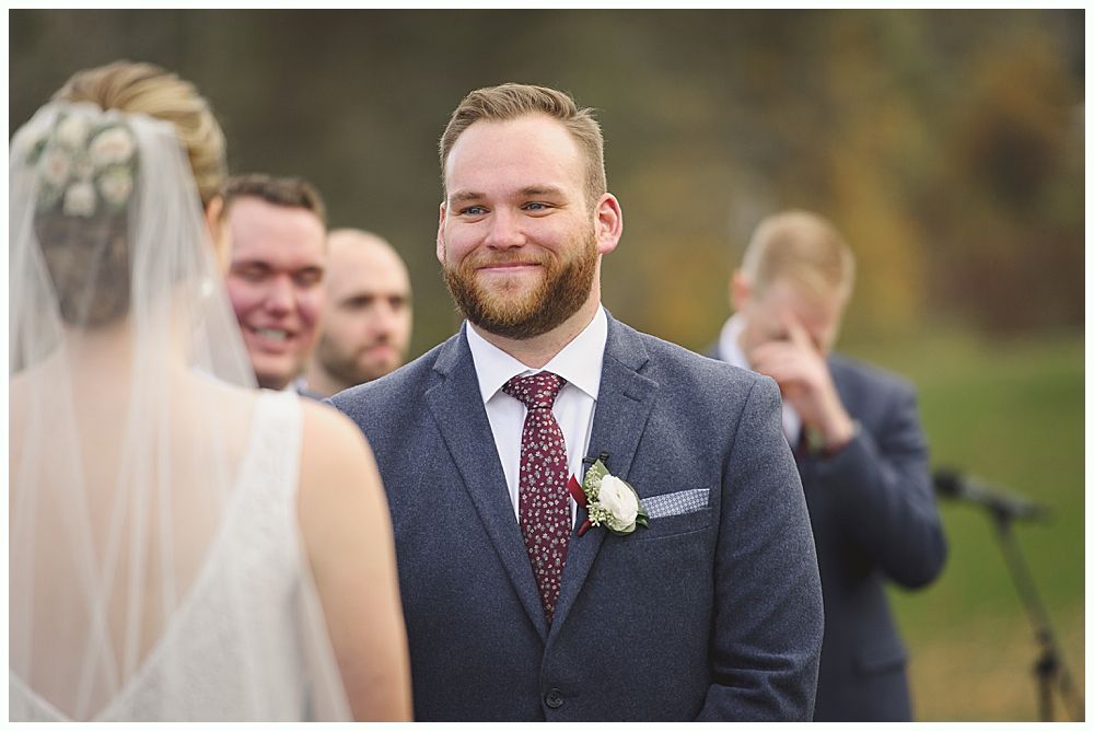 Couple embracing, noses touching, looking at each other. Snowy outdoor setting. Woman's hand with engagement ring visible.