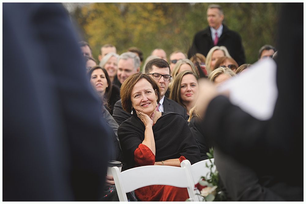 Woman in a crowd, smiling and resting her chin on her hand, at an outdoor event.