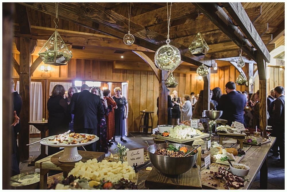 Barn interior with guests, food tables, and hanging glass globe lights.