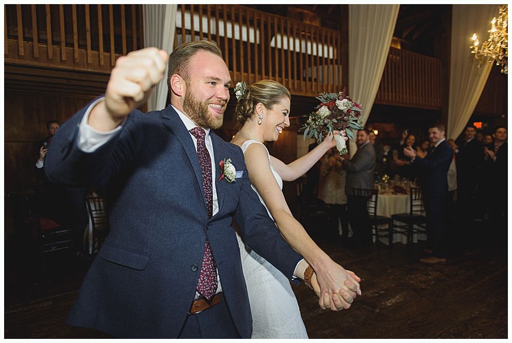 Woman in red gown throws bouquet at wedding reception. Man in suit reaches for it. Wooden interior.