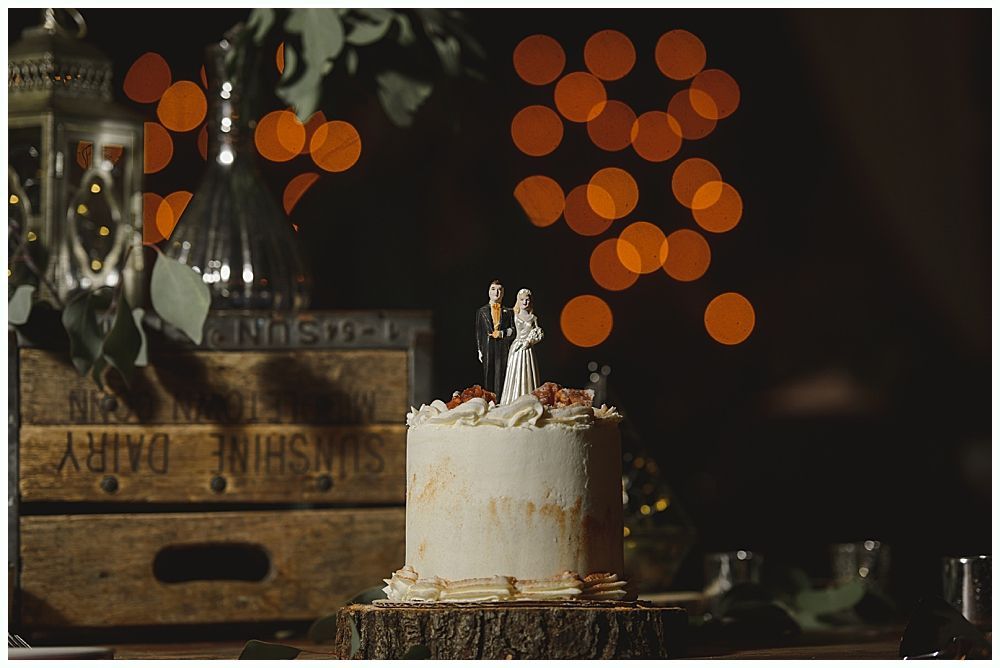 Wedding cake with figurines, on a wood slice. Rustic decor with blurred lights in the background.