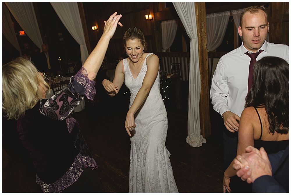 Bride dancing at a wedding reception, other guests visible in dimly lit room.