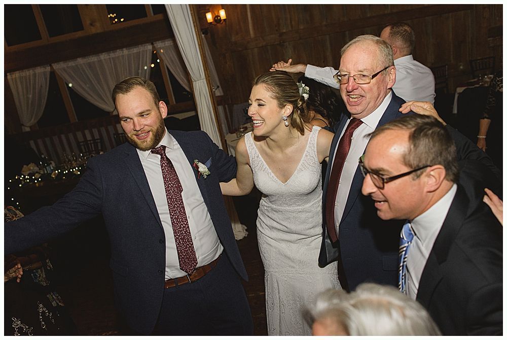 A wedding reception: Bride and groom dance joyfully with guests in a rustic setting, everyone smiling.