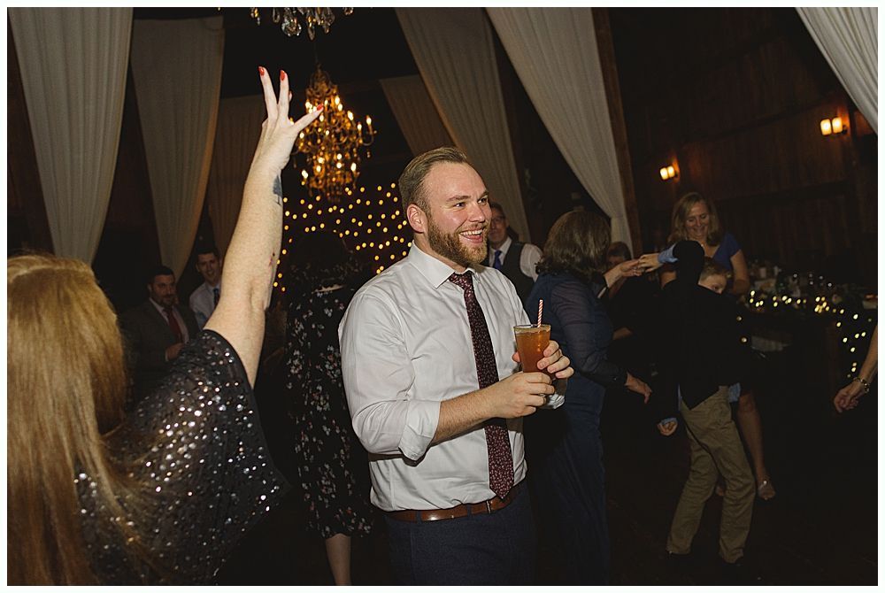 People dancing at a party; man in a striped shirt holding a drink smiles.
