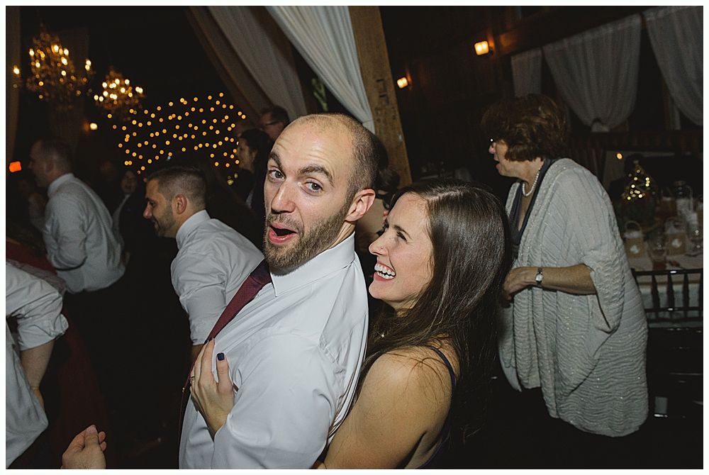 Couple dancing closely, man with surprised expression, woman laughing, party setting with lights.