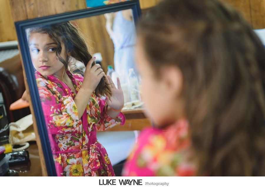 Girl in floral robe looks in mirror, touching her wavy hair.