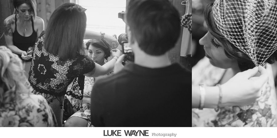 Woman adjusting bride's veil. Bride is wearing floral dress. Others are in the background. Black and white.